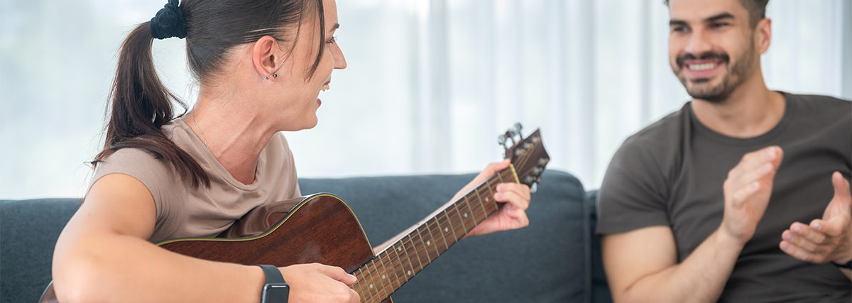 Eine Frau spielt Gitarre während ein Mann ihr glücklich zuhört