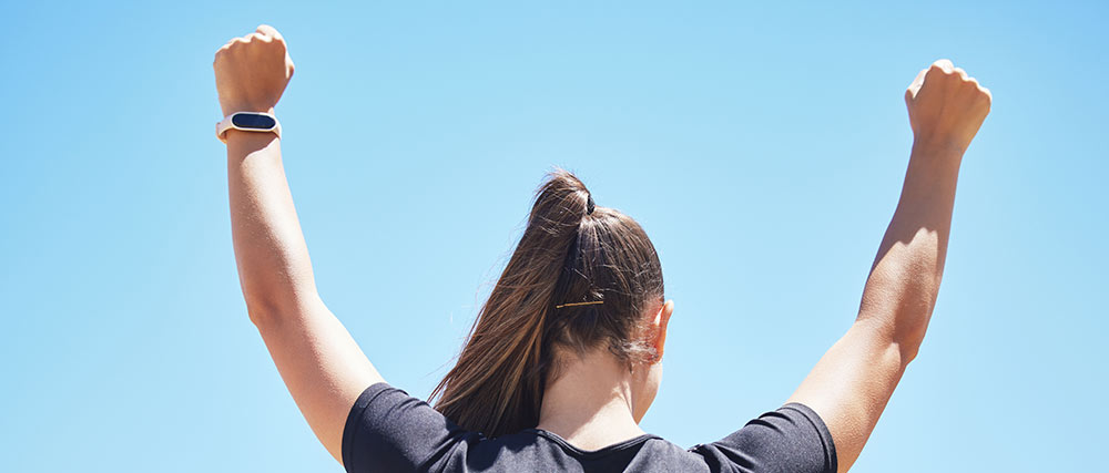 Frau von hinten mit erhobenen Armen vor blauem Himmel