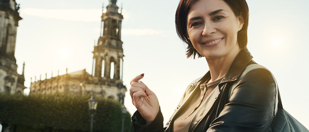 Lächelnde Frau in der Stadt mit historischer Kirche im Hintergrund bei Sonnenlicht