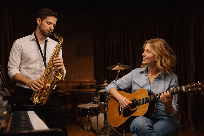 Erwachsene lernen Musik: Mann spielt Saxophon und Frau spielt Gitarre in einem Musikstudio