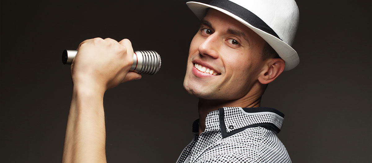 Lächelnder Mann, der mit Hut in ein Mikrofon singt