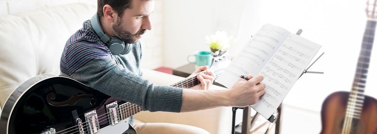 Mann mit Gitarre schreibt Musiknoten auf Papier