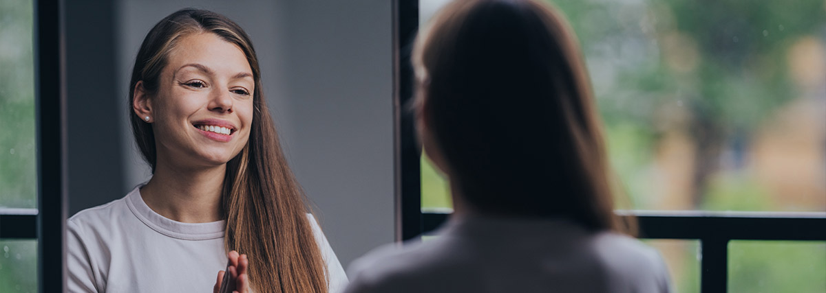 A smiling woman looking at herself in the mirror