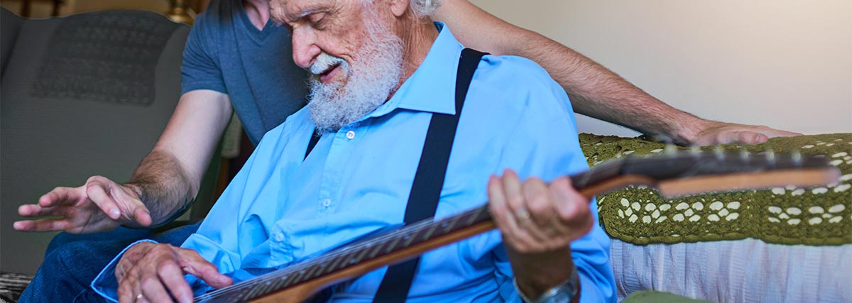 Mann bringt einer Seniorin das Spielen der E-Gitarre bei